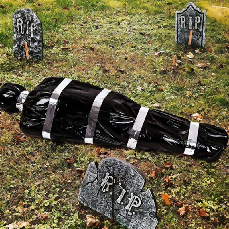 Scary fake corpse in bag Halloween outdoor prop displayed in yard with gravestone